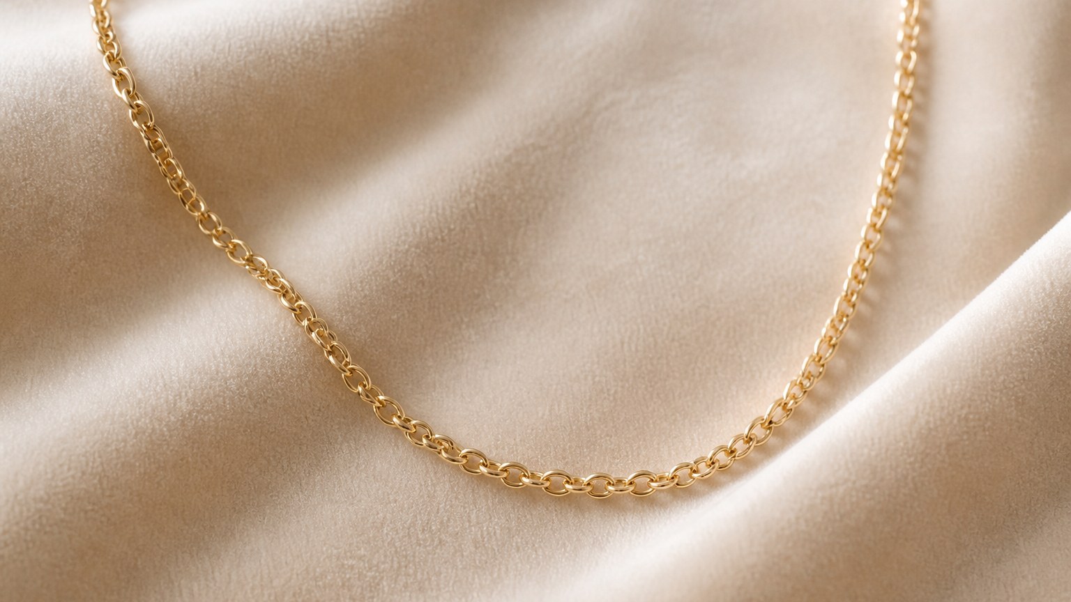 Chaîne fine en or 18 carats maille forçat posée sur un tissu beige
